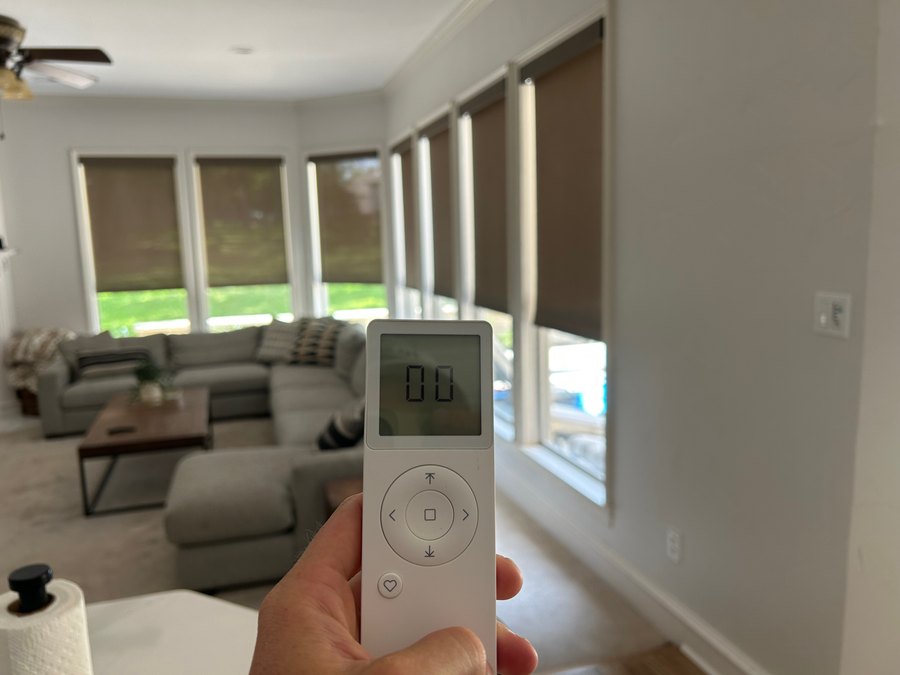 Homeowner using a handheld remote to control motorized roller shades by Love Is Blinds